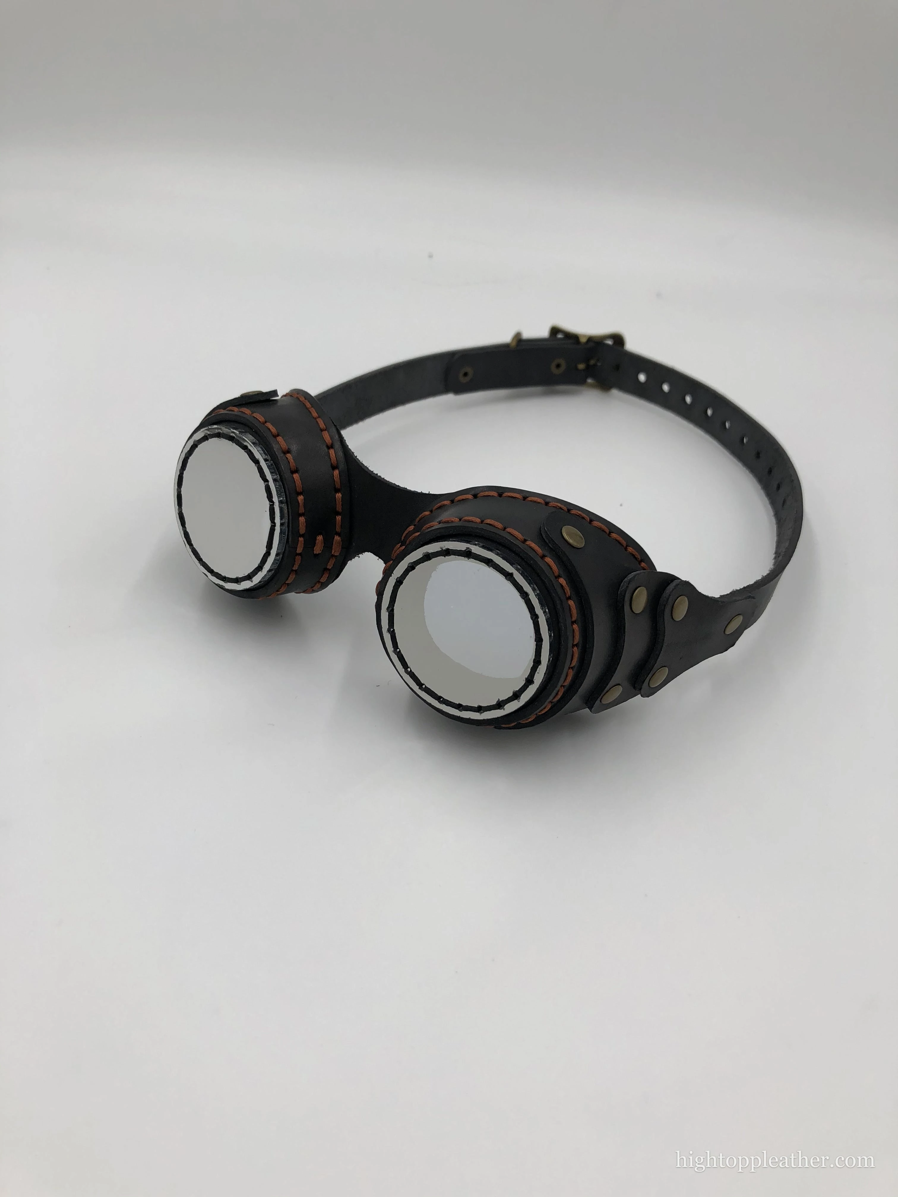 Black leather aviator goggles with copper-orange contrast stitching and brass hardware.
