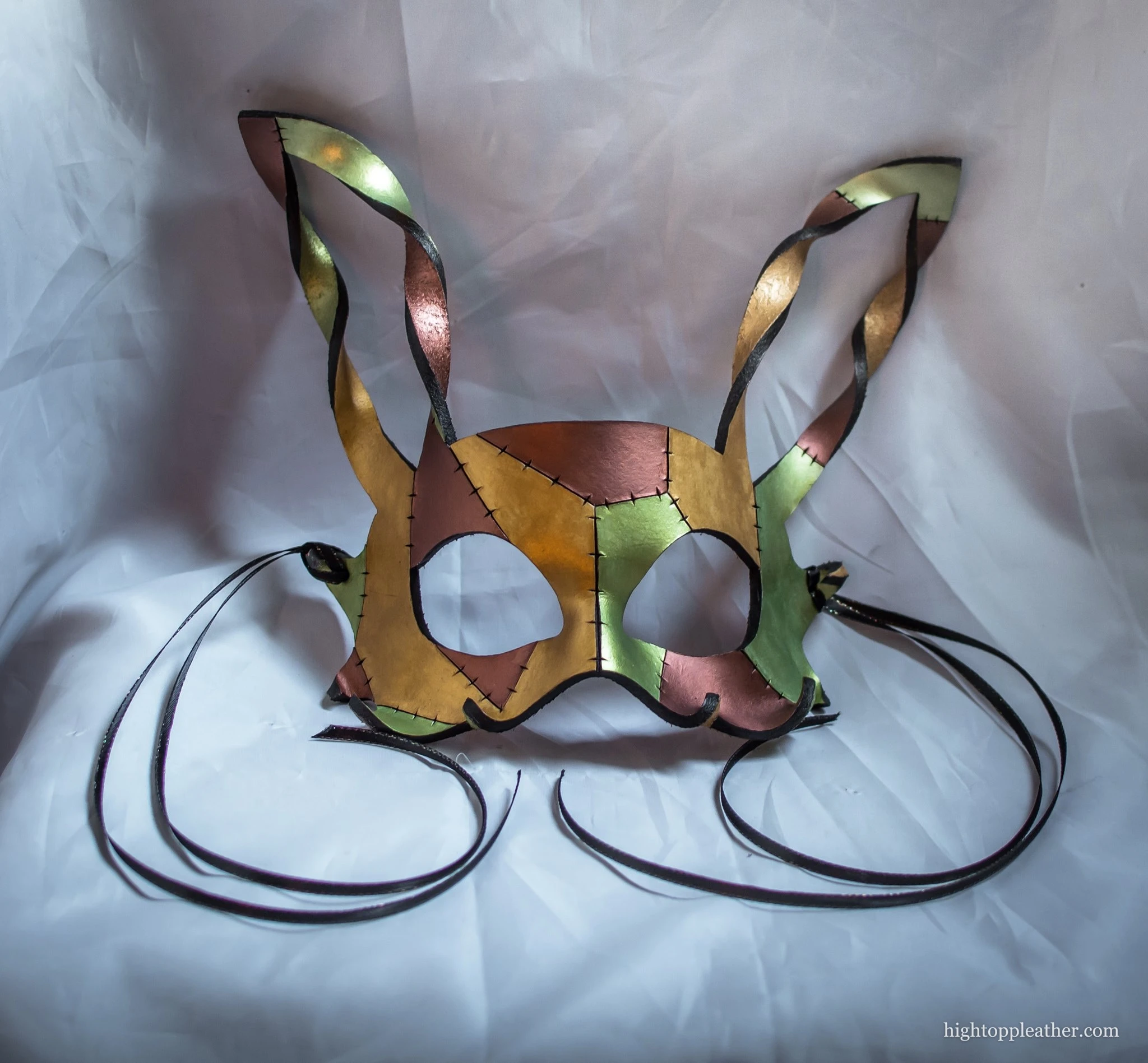 Leather hare mask with tall ears, painted in metallic copper, gold, and green.