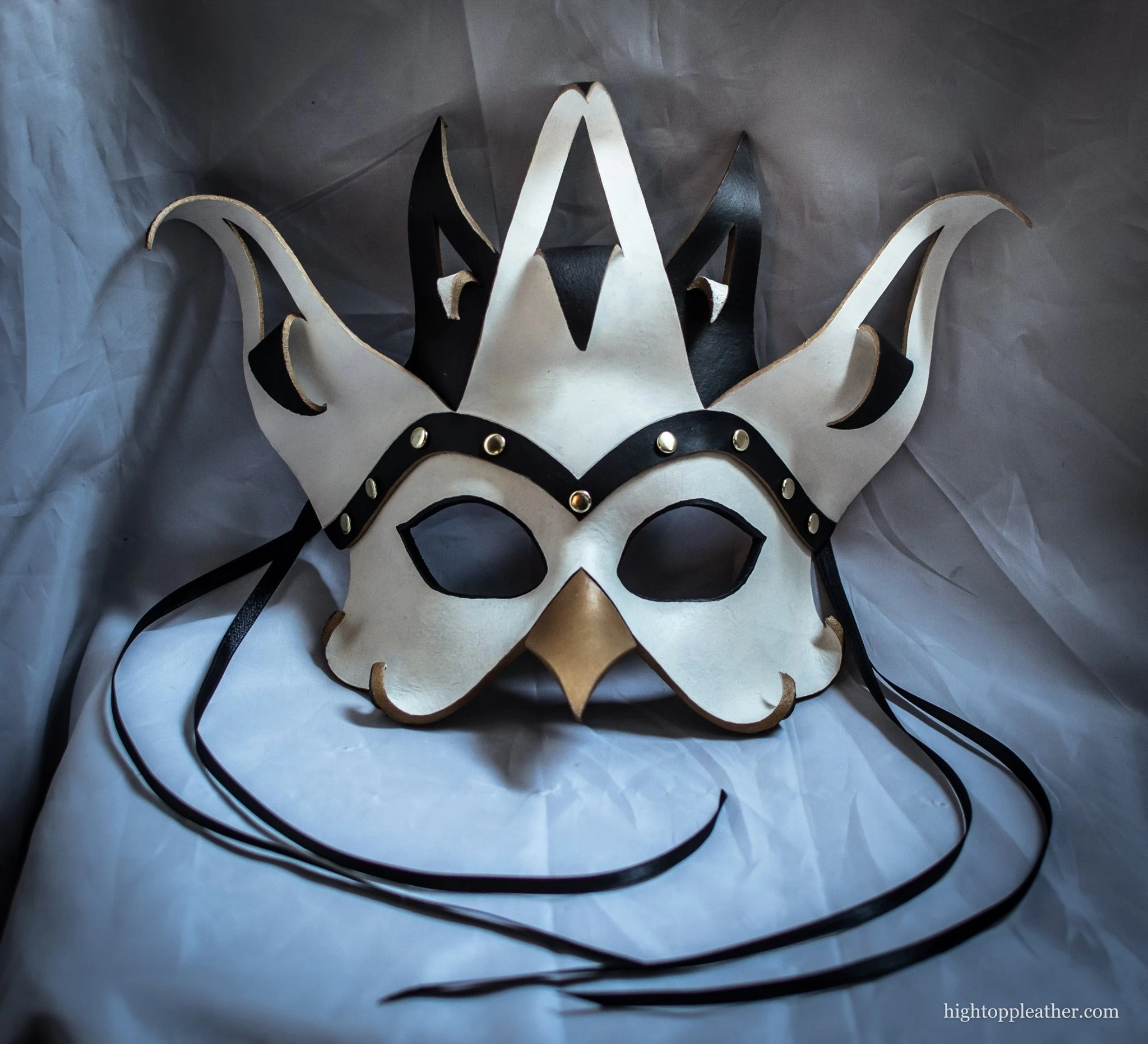 White and black leather mask with gold accents and a crown of pointed horns.