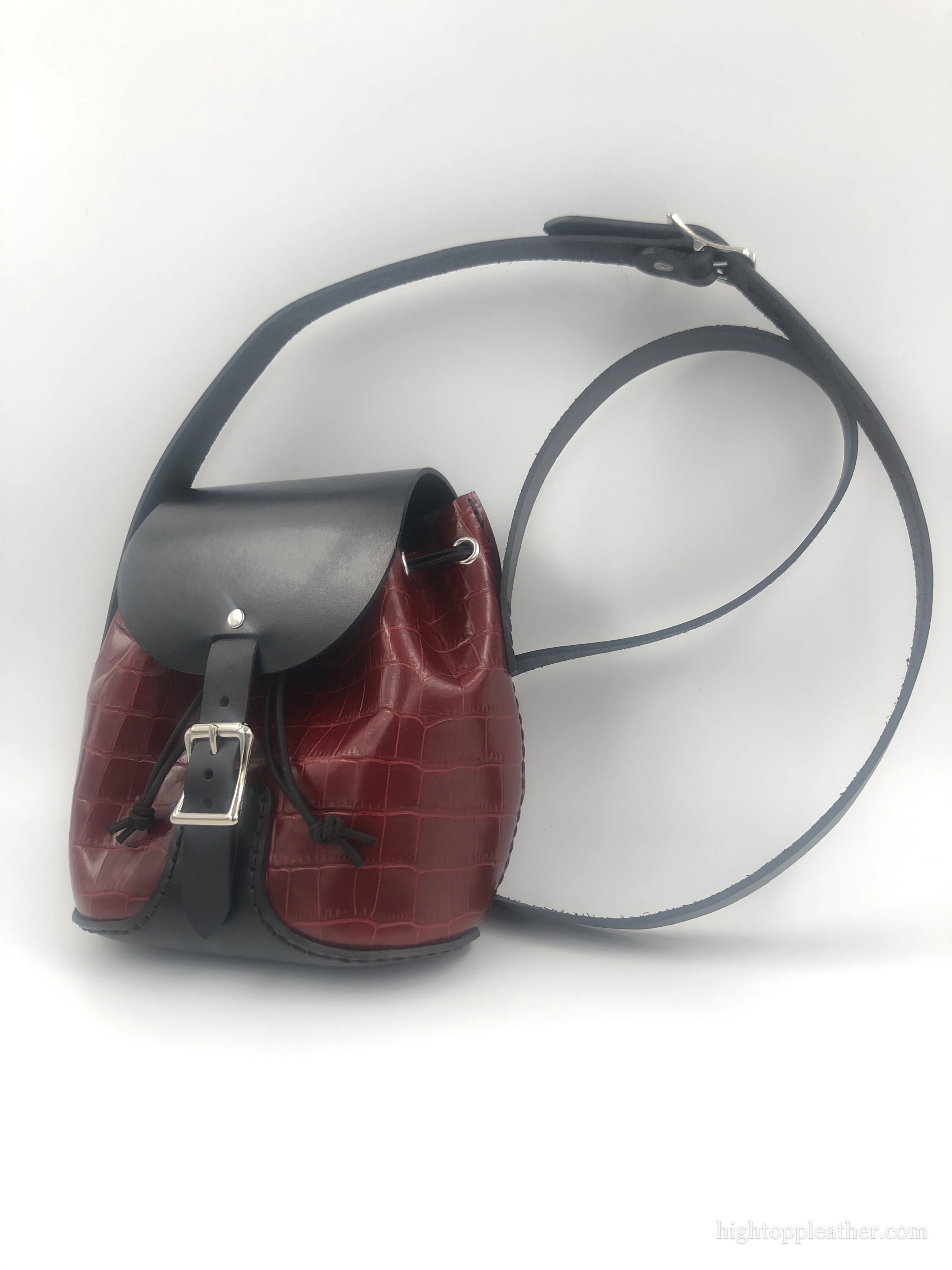 Oxblood crossbody satchel in embossed leather with a black flap and adjustable strap.