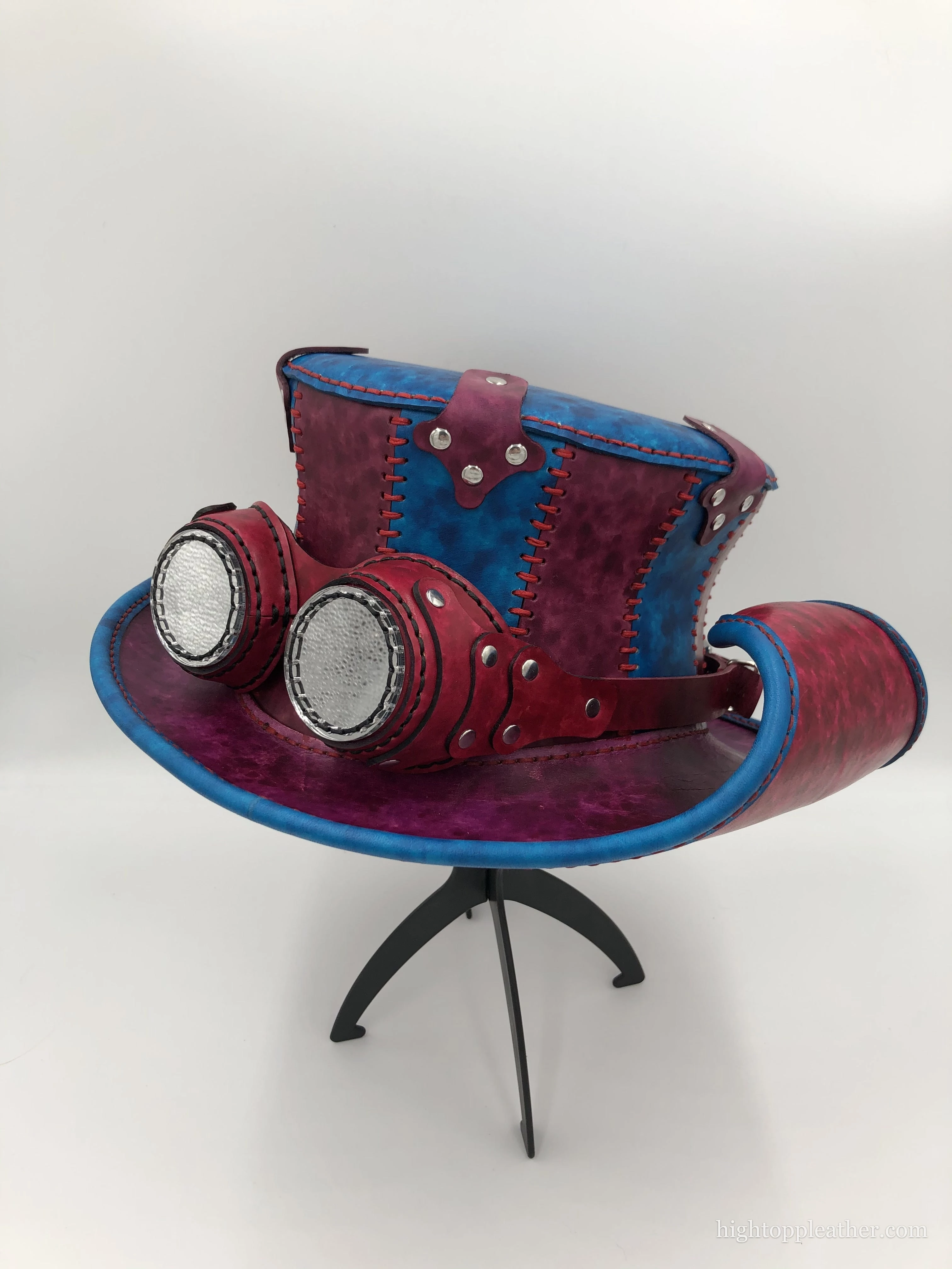 Steampunk leather top hat in oxblood and electric blue, with matching goggles wrapped around the brim.